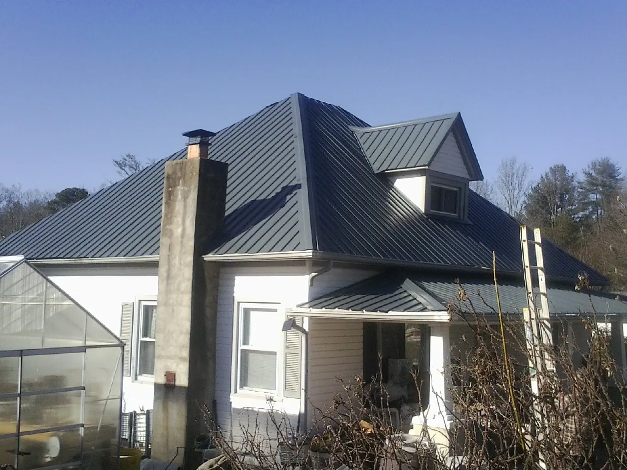 Dark blue standing seam metal roof on a white farmhouse with dormer — Slate & Tile Roof Repair by Roofing Brothers in Dallas Center