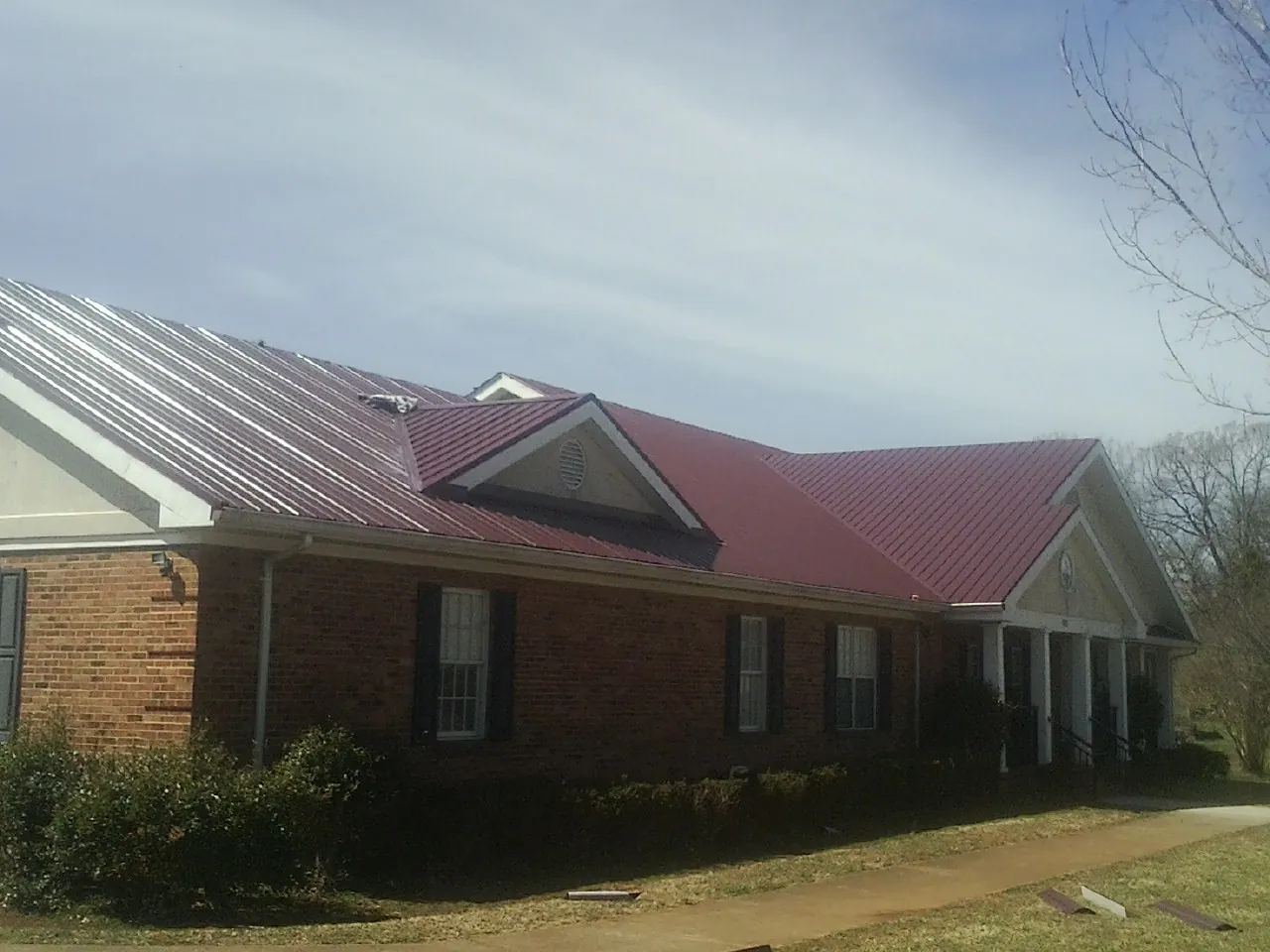 Red metal roof with gabled entries on a long brick building, from a Hail Damage Roof Repair job in Dallas Center