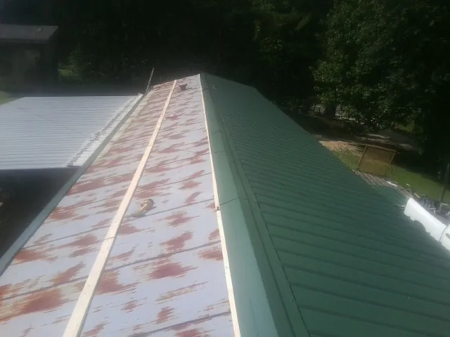 Old rusted panels beside newly installed green metal roofing — Wind Damage Roof Repair by Roofing Brothers in Dallas Center