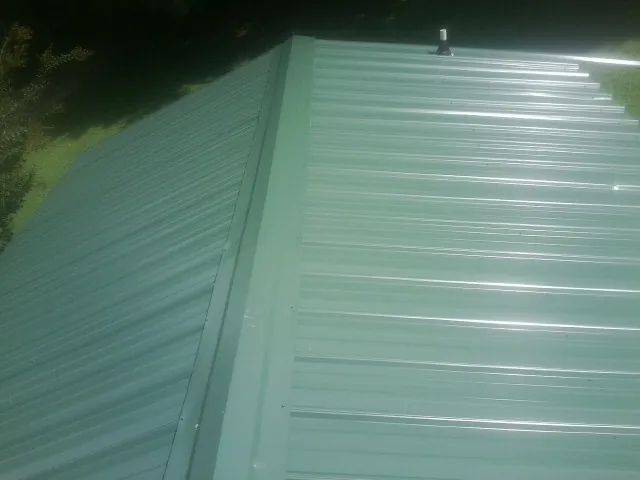 New green metal panels meeting at the ridge of a roof — Flat Roof Repair work by our crew in Dallas Center