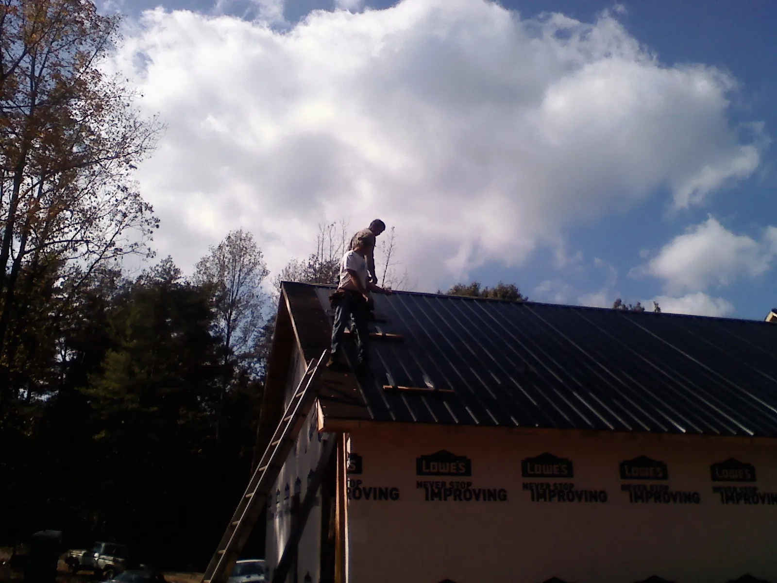Roofer fastening dark metal panels high against a cloudy sky, from a Roof Inspection job in Dallas Center