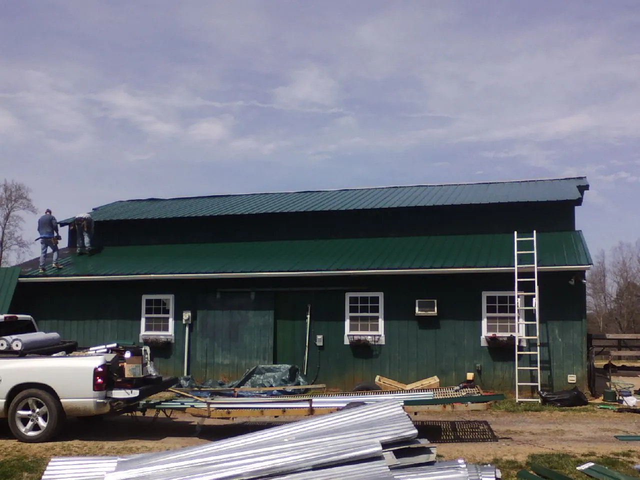 Crew installing green metal roofing on a large green barn in Dallas Center