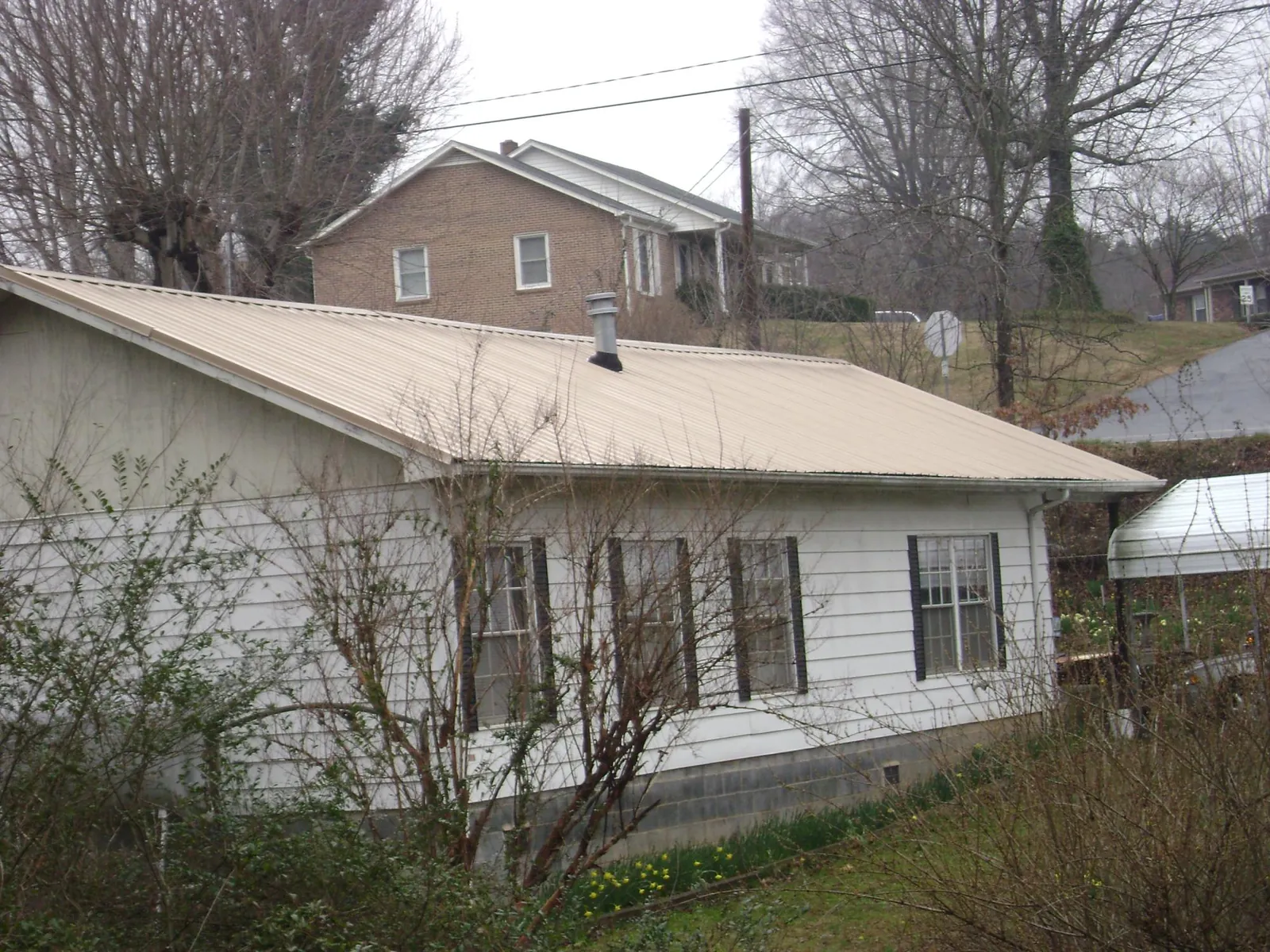 Tan metal roof on a white sided house set into a hillside — Commercial Roofing by Roofing Brothers in Dallas Center