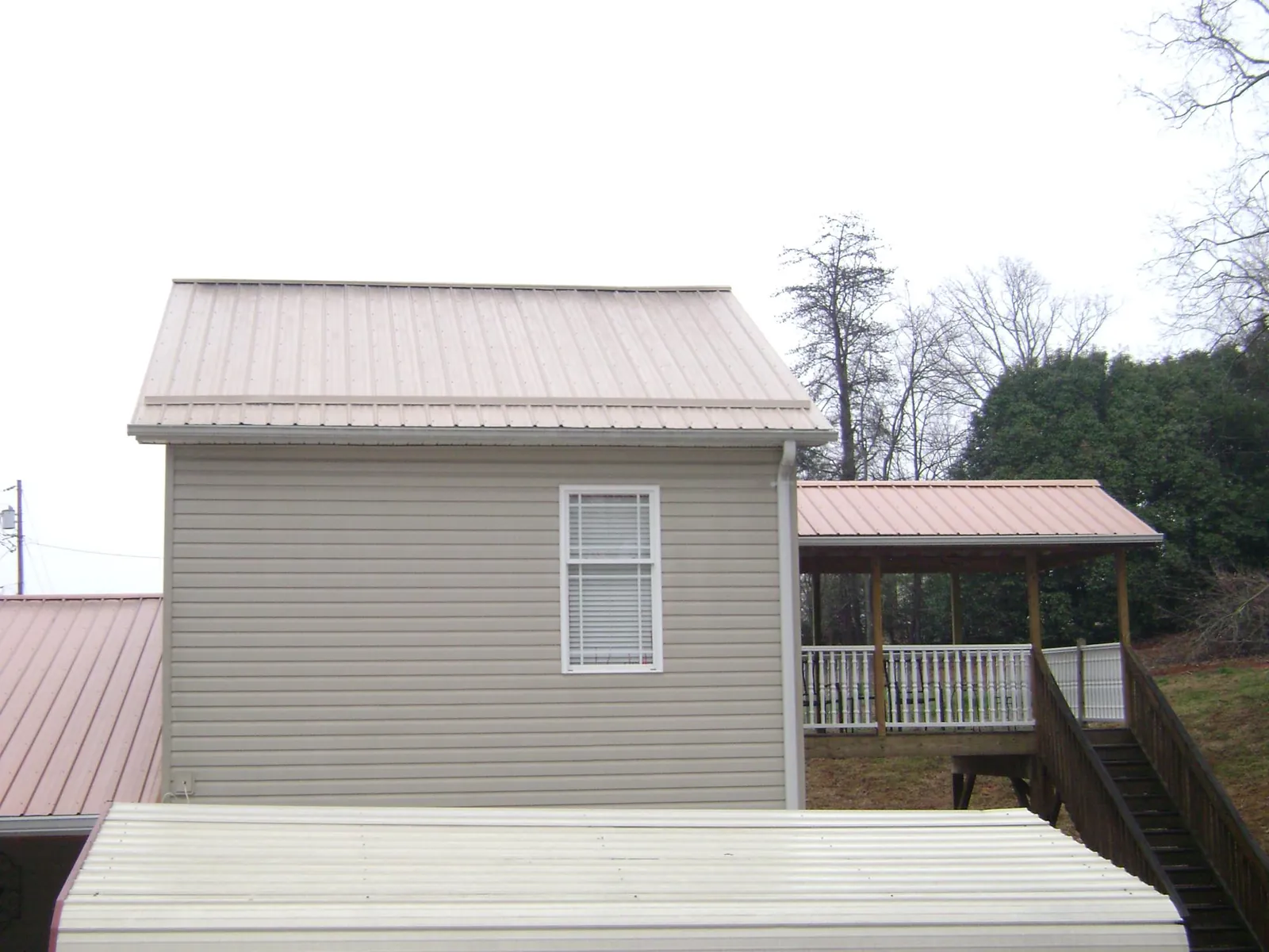 Tan metal roofs on a two story addition and attached porch, from a Roof Replacement job in Dallas Center