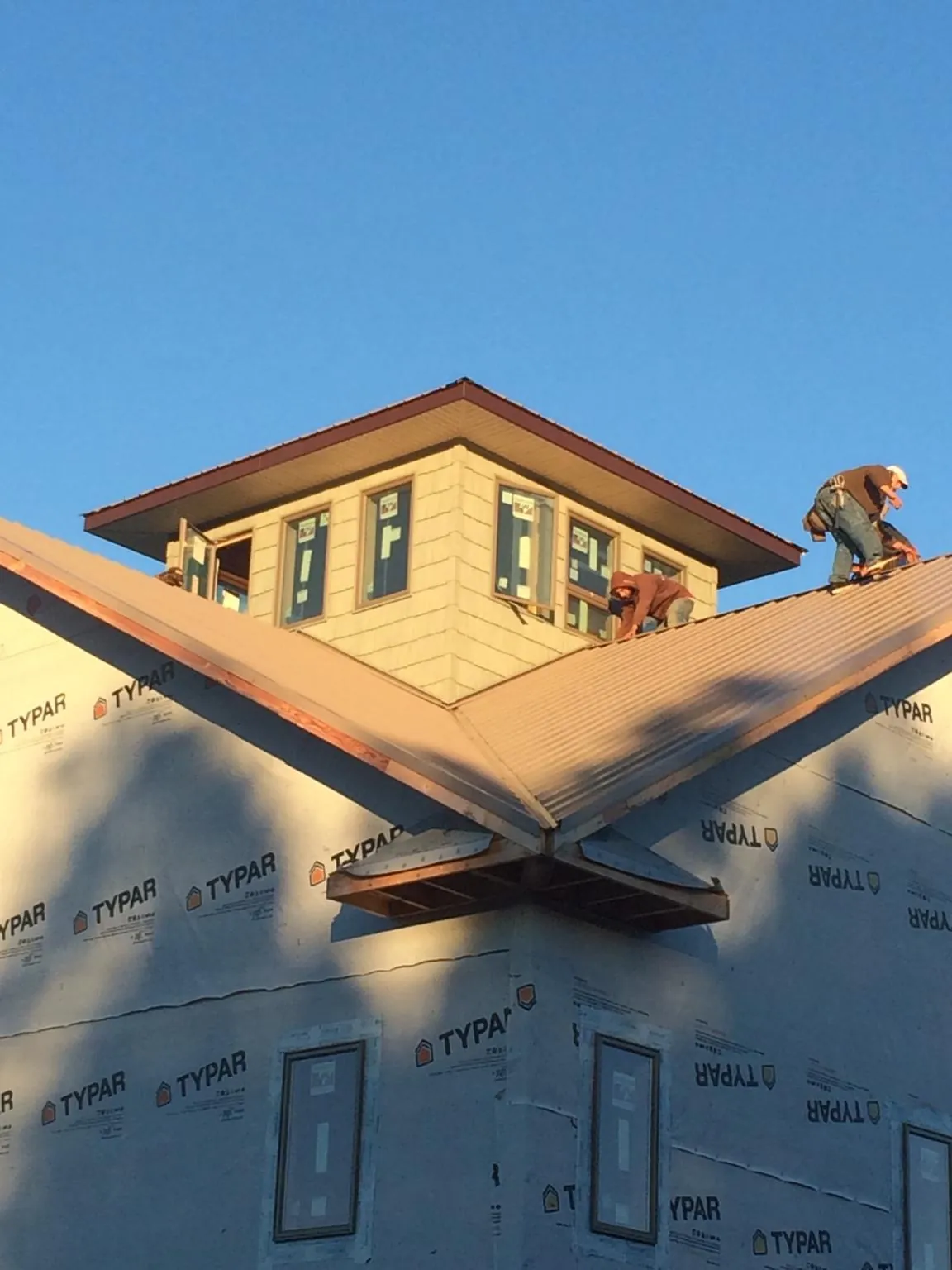 Roofers working around a rooftop cupola on a new metal roof at sunset — Roof Waterproofing in Dallas Center by Roofing Brothers